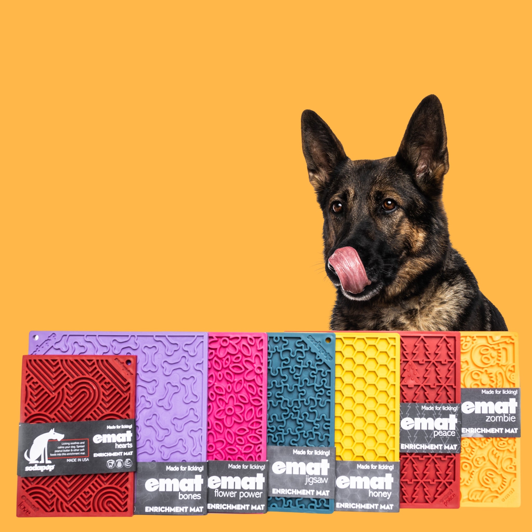 German Shepherd licking lips beside colorful eMat dog enrichment mats with heart, bone, honeycomb, and puzzle textures
